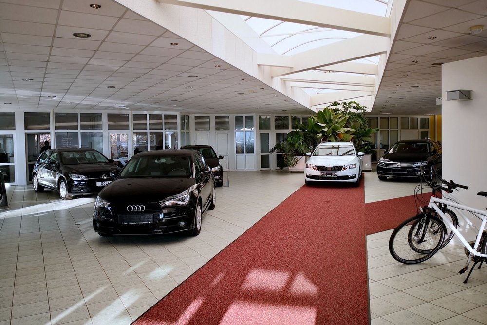 Innenansicht eines Autohauses mit mehreren ausgestellten Fahrzeugen und roten Teppichwegen.