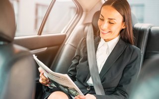 Frau im Business-Outfit liest auf dem Rücksitz eines Autos eine Zeitung.