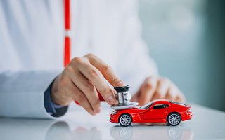 Person untersucht ein rotes Spielzeugauto mit einem Stethoskop – symbolisch für eine Fahrzeugdiagnose.