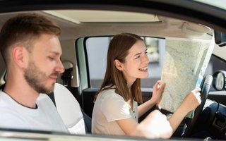 Zwei Personen sitzen im Auto, die Beifahrerin hält eine Straßenkarte.