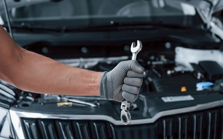 Mechaniker hält Schraubenschlüssel vor geöffnetem Motorraum eines Autos.