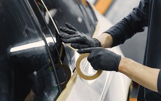 Person mit schwarzen Handschuhen klebt Abdeckband entlang einer Autoscheibe.